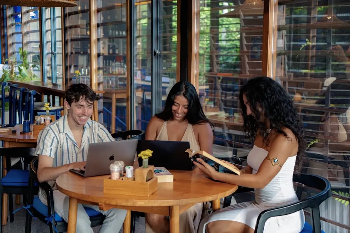 Three people working on laptops at a bright Bali cafe, suitable for remote workers seeking a comfortable workspace.