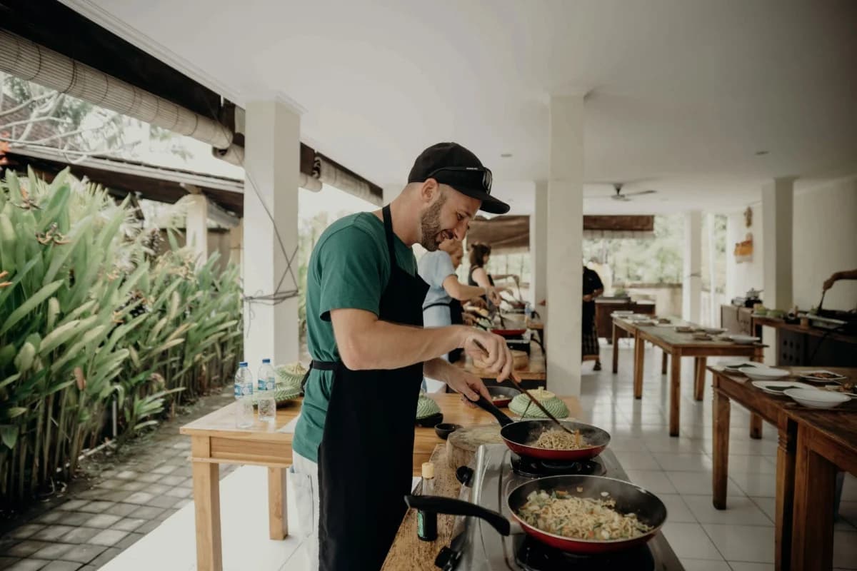 Traveler preparing Balinese food during a cooking class, with other participants cooking in an open-air kitchen.